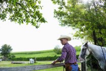 Young man in cowboy gear with horse checking fence — Stock Photo