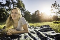 Портрет молодой женщины, лежащей на одеяле для пикника в парке — стоковое фото