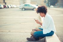 Mulher jovem mensagens de texto no smartphone no estacionamento da cidade — Fotografia de Stock