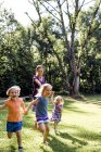 Середня доросла жінка біжить і тримає руки з трьома дочками в парку — стокове фото