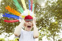 Niño en tocado de plumas gritando en el jardín - foto de stock