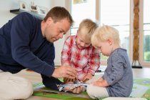 Mittlerer erwachsener Mann und zwei Söhne bereiten Spielzeugflugzeug auf Wohnzimmerboden vor — Stockfoto