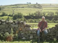 Farmer sitting by dry stone wall in field — Stock Photo