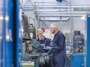 Senior engineer instructing apprentice on factory machinery — Stock Photo