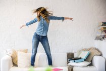 Junge Frau steht tanzend auf Sofa und schüttelt ihre Haare — Stockfoto