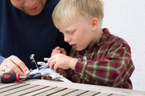 Середній дорослий чоловік і син готують іграшковий літак на столі з патіо — стокове фото