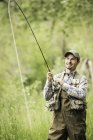 Uomo che indossa trampolieri pesca, sorridente — Foto stock