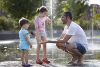Mitte erwachsener Mann und zwei Töchter spielen in Wasserfontänen, Madrid, Spanien — Stockfoto