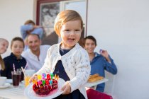 Female toddler carrying birthday cake on patio — Stock Photo