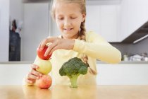 Girl building tower of apples and broccoli — Stock Photo
