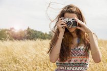 Junge Frau fotografiert mit Oldtimer-Kamera im Feld — Stockfoto
