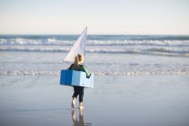 Дівчина біжить з іграшковим човном у море — стокове фото