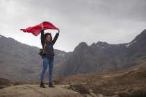 Mujer con bandera roja en las montañas, Piscinas de hadas, Isla de Skye, Hébridas, Escocia - foto de stock