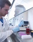 Cientista usando a pipeta do multi poço para encher a placa do multi poço no armário biológico da segurança no laboratório — Fotografia de Stock