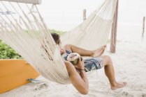 Человек наслаждается кокосовой водой в гамаке на пляже — стоковое фото