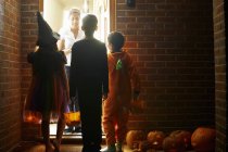 Rear view of children wearing Halloween costumes trick or treating — Stock Photo
