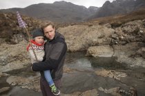 Padre sosteniendo hijo, Piscinas de hadas, Isla de Skye, Hébridas, Escocia - foto de stock