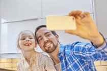 Father and daughter taking selfie in kitchen — Stock Photo