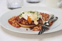 Poached egg, bacon and beans with hollandaise sauce on english muffin — Stock Photo