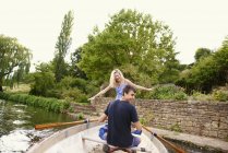 Rear view of young woman with boyfriend standing in rowing boat on river — Stock Photo
