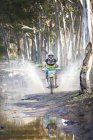 Young male motocross racer splashing through puddle in forest — Stock Photo