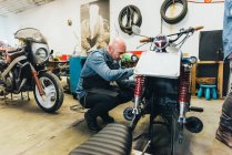 Зрілий чоловік, що працює на мотоциклі в гаражі — стокове фото