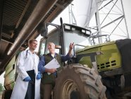 Farmer with clipboard in discussion with vet by tractor on dairy farm — Stock Photo