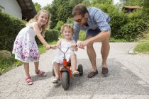 Ragazza in sella triciclo con padre e sorella — Foto stock