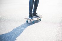 Piernas de skateboarder urbano masculino virar skateboarding en carretera - foto de stock