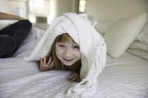 Молодая девушка выглядывает из-под одеяла на кровать — стоковое фото