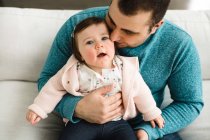 Bébé fille levant les yeux tout en étant blotti par son père — Photo de stock