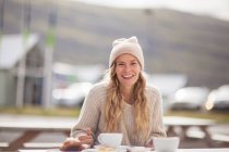 Portrait of female tourist in knit hat having coffee on picnic bench, Seyoisfjorour, Iceland — Stock Photo