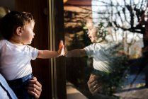 Menino nos braços do pai olhando através e tocando janela — Fotografia de Stock