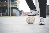 Jeune pied masculin sur le ballon de football dans la rue de la ville — Photo de stock
