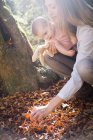 Mãe e filha agachado investigando folhas no chão da floresta — Fotografia de Stock