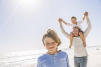 Father and sons on beach, carrying on shoulders smiling — Stock Photo