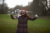 Mujer en el parque usando varita de burbujas para hacer burbujas - foto de stock