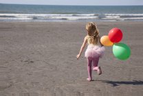 Chica en la playa con tutú sosteniendo globos, Gales, Reino Unido - foto de stock