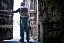 Vue arrière du forgeron masculin ouvrant la porte de la grange traditionnelle, Cagliari, Sardaigne, Italie — Photo de stock