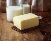 Bloque de mantequilla con botellas de leche sobre mesa de madera - foto de stock