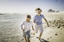 Hermanos corriendo en la playa - foto de stock