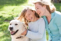 Мати і дочка в саду з собакою посміхаються — стокове фото