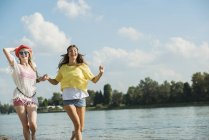 Two female friends running by lake — Stock Photo