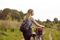Young woman with bicycle looking over her shoulder from rural dirt track — Stock Photo