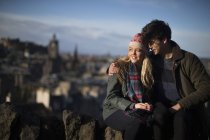 Una joven pareja se abraza en Calton Hill con el trasfondo de la ciudad de Edimburgo, capital de Escocia - foto de stock