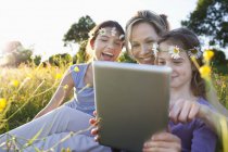 Madre e hijas usando tableta digital en el campo - foto de stock