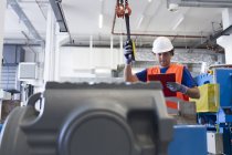 Mid adult man wearing hard hat operating machine, looking down at clipboard — Stock Photo