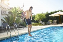 Jovem usando óculos de natação pulando na piscina — Fotografia de Stock