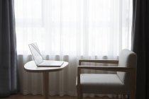 Ноутбук на столе со стулом, перед окном — стоковое фото