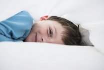 Porträt eines Jungen, der zwischen weißen Bettlaken liegt — Stockfoto